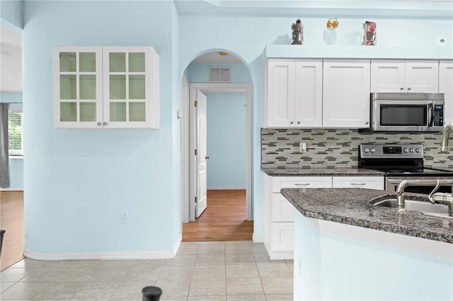 kitchen featuring white cabinets, stainless steel appliances, light wood-type flooring, and dark stone countertops