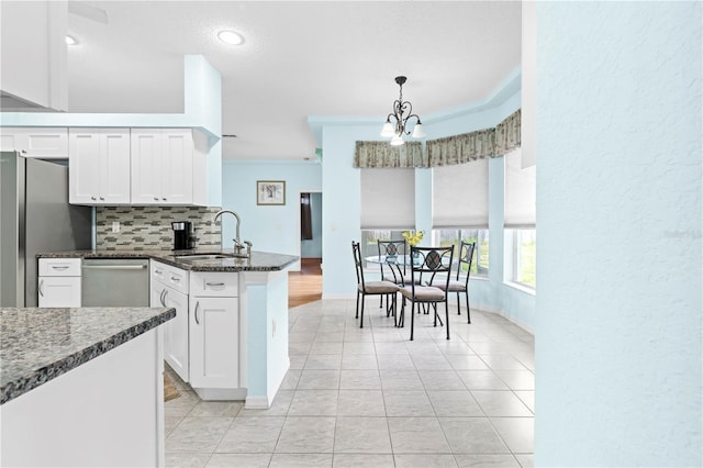 kitchen featuring sink, white cabinetry, stainless steel appliances, pendant lighting, and dark stone countertops