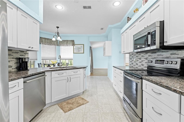 kitchen featuring dark stone counters, sink, crown molding, white cabinets, and appliances with stainless steel finishes