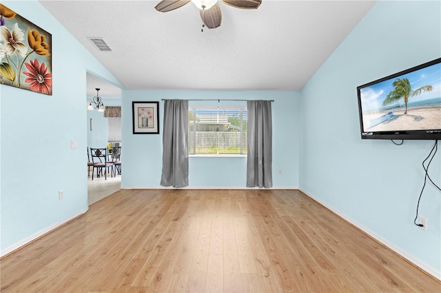 empty room featuring a textured ceiling, vaulted ceiling, ceiling fan with notable chandelier, and light hardwood / wood-style floors