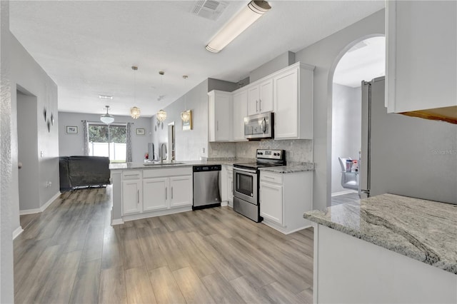 kitchen featuring kitchen peninsula, white cabinetry, decorative light fixtures, and appliances with stainless steel finishes