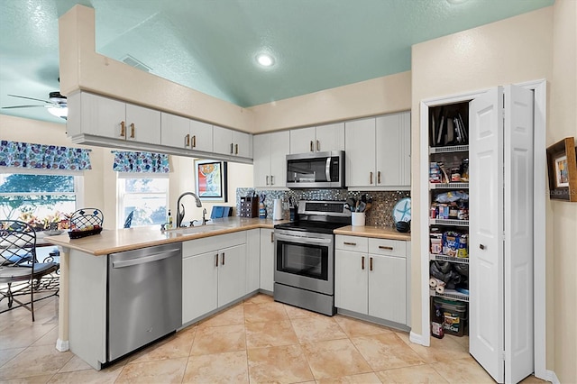 kitchen with kitchen peninsula, white cabinets, backsplash, sink, and stainless steel appliances