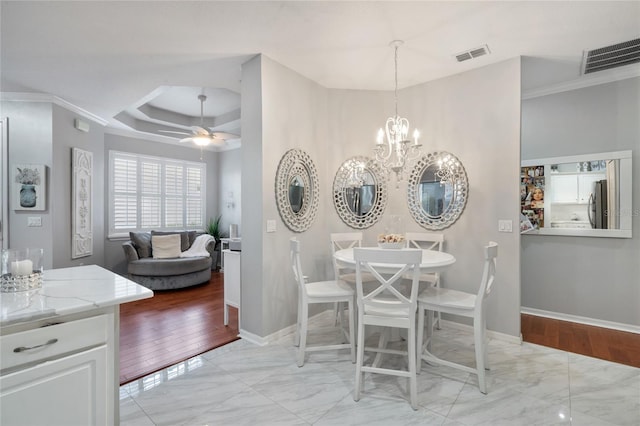 dining space with ceiling fan with notable chandelier, a tray ceiling, light hardwood / wood-style flooring, and crown molding