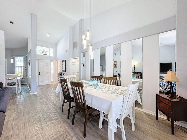 dining space with high vaulted ceiling and light wood-type flooring