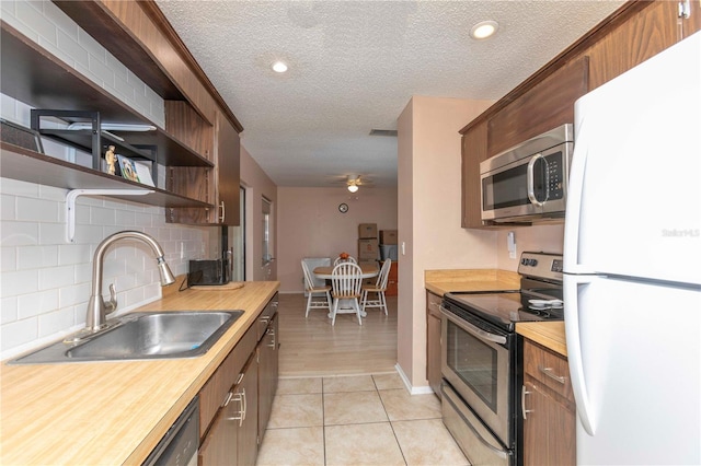 kitchen with appliances with stainless steel finishes, a textured ceiling, light hardwood / wood-style flooring, wooden counters, and sink