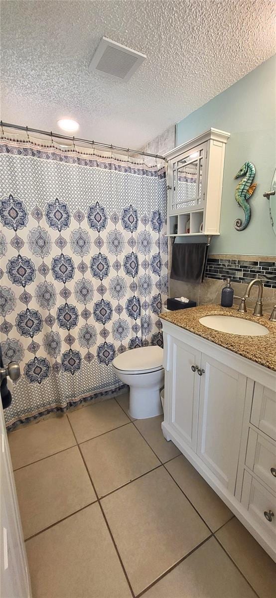 bathroom featuring tile patterned flooring, vanity, toilet, and a textured ceiling