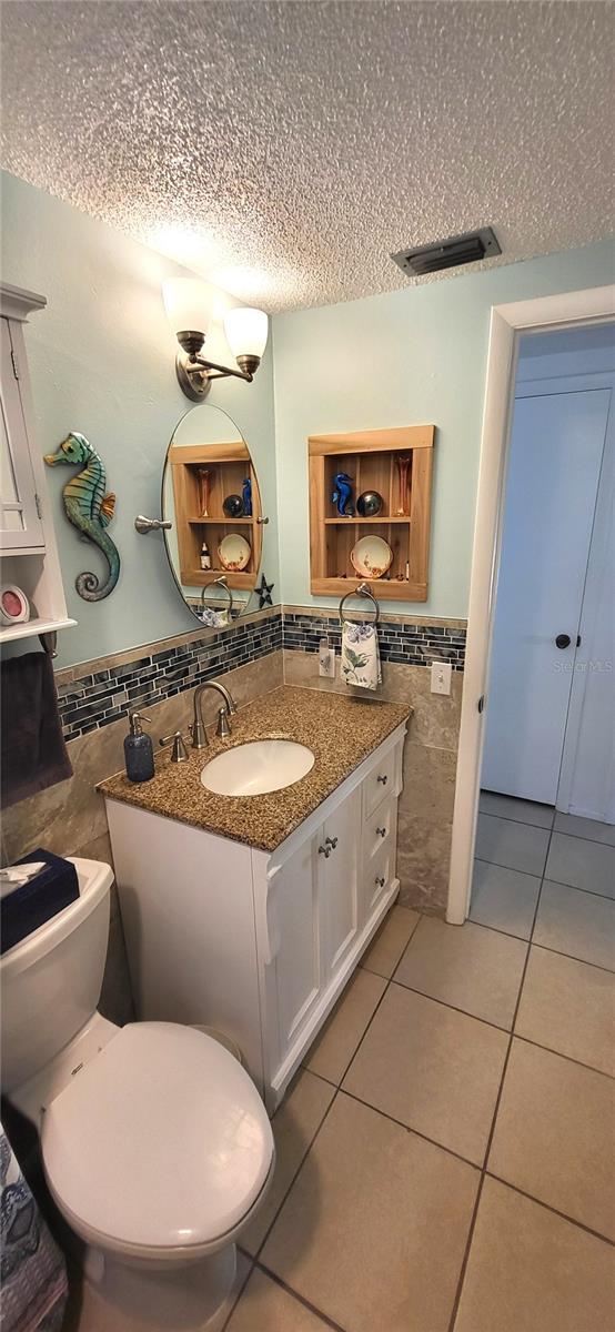 bathroom with vanity, a textured ceiling, tile walls, tile patterned flooring, and toilet