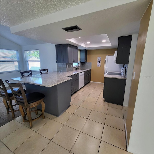 kitchen with kitchen peninsula, a tray ceiling, dishwashing machine, a breakfast bar, and light tile patterned floors