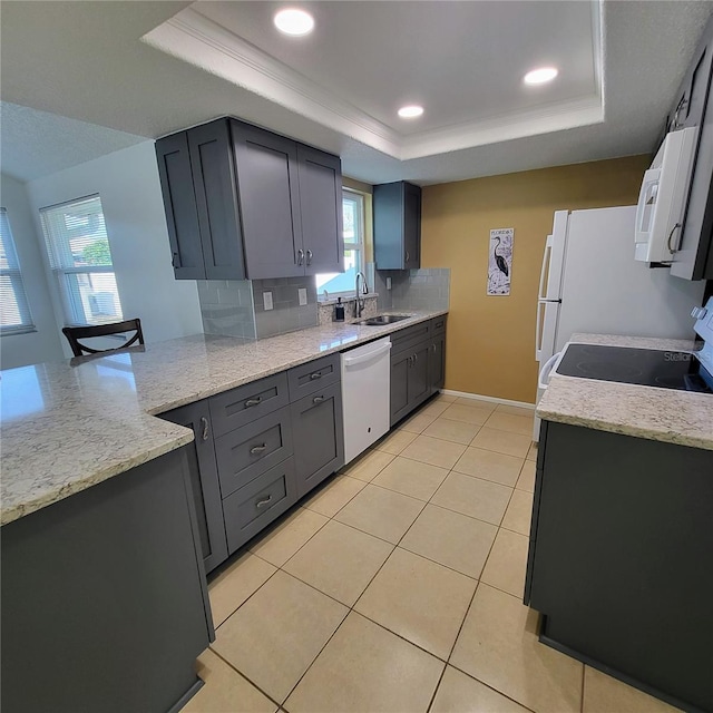 kitchen with backsplash, light stone counters, a tray ceiling, sink, and dishwasher