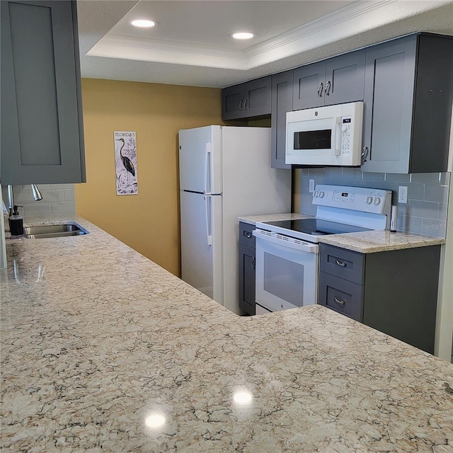 kitchen with sink, white appliances, a tray ceiling, and backsplash