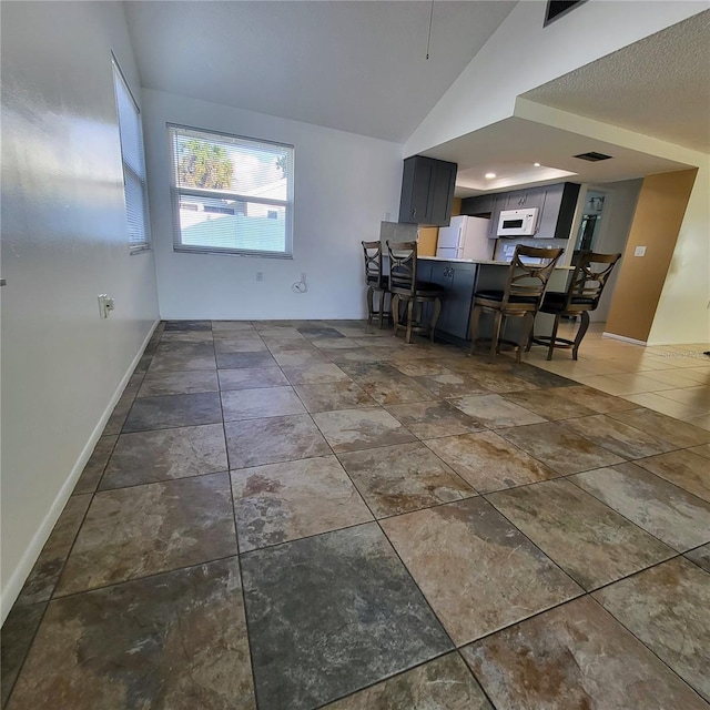 kitchen with a breakfast bar, white appliances, and vaulted ceiling