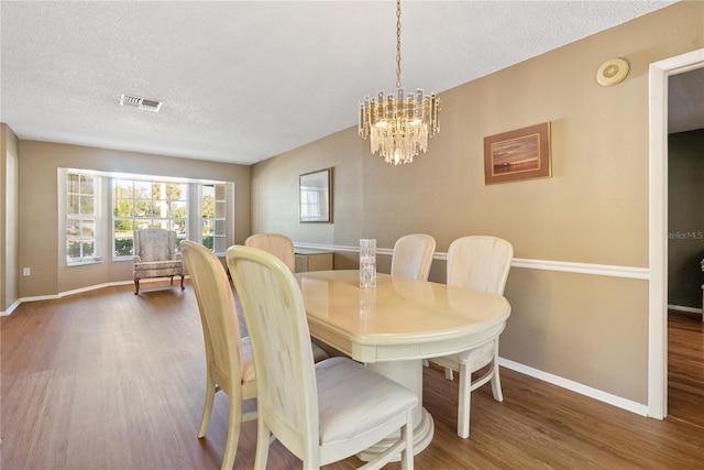 dining room featuring dark wood-type flooring, a textured ceiling, and an inviting chandelier