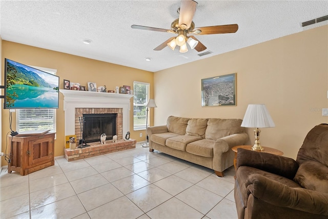 living room featuring a textured ceiling, ceiling fan, light tile patterned floors, and a brick fireplace