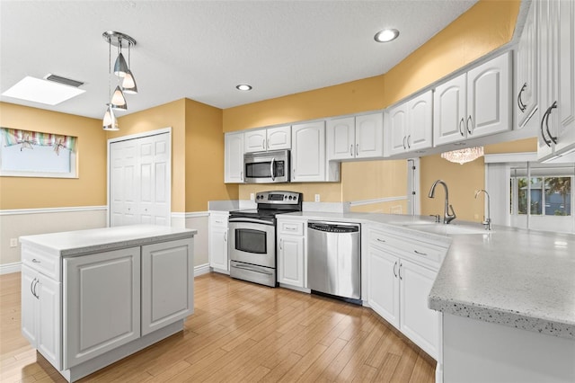 kitchen with sink, appliances with stainless steel finishes, decorative light fixtures, and white cabinetry