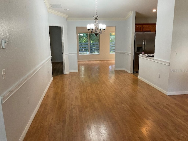 unfurnished dining area featuring crown molding, wood-type flooring, and an inviting chandelier