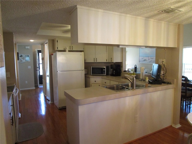 kitchen with kitchen peninsula, a textured ceiling, dark hardwood / wood-style floors, sink, and white appliances