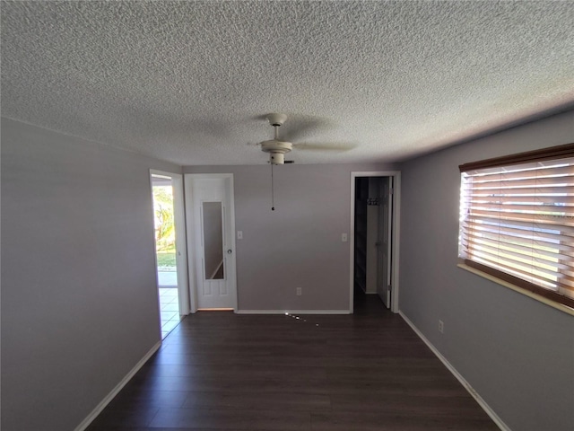 spare room featuring a healthy amount of sunlight, a textured ceiling, ceiling fan, and dark wood-type flooring