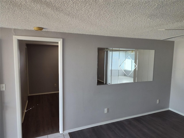 empty room with a textured ceiling, wood finished floors, and baseboards