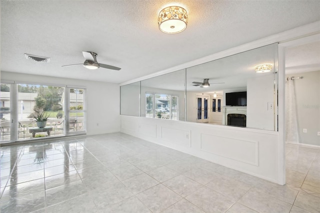 unfurnished living room with ceiling fan, tile patterned floors, and a textured ceiling