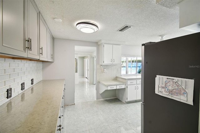 kitchen featuring backsplash, stainless steel fridge, light tile patterned floors, white cabinets, and a textured ceiling