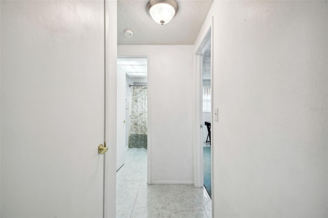 hallway with a textured ceiling and light tile patterned floors