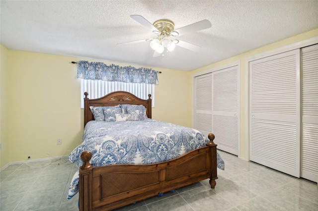 tiled bedroom with two closets, a textured ceiling, and ceiling fan