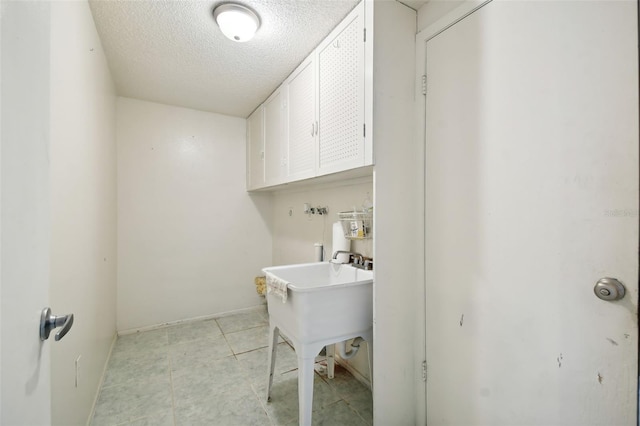 clothes washing area featuring a textured ceiling and cabinets