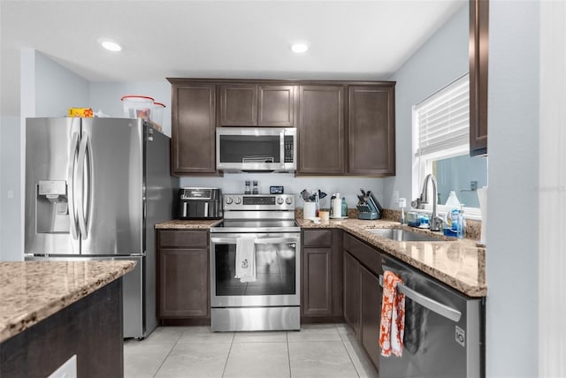 kitchen with light stone counters, sink, light tile patterned floors, and stainless steel appliances