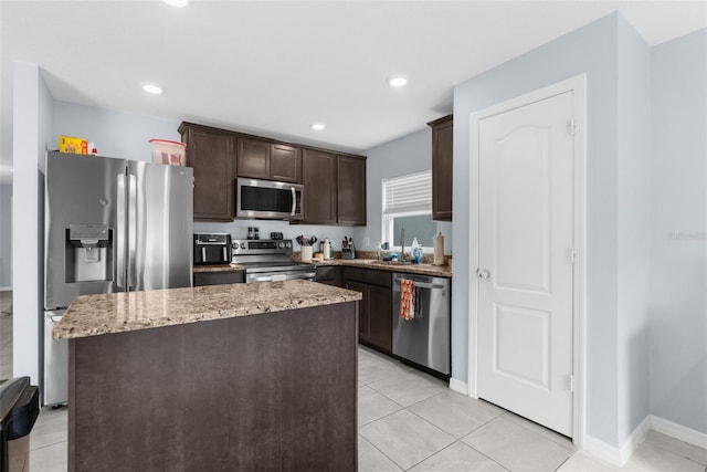 kitchen featuring dark brown cabinetry, a center island, stainless steel appliances, light stone counters, and light tile patterned floors