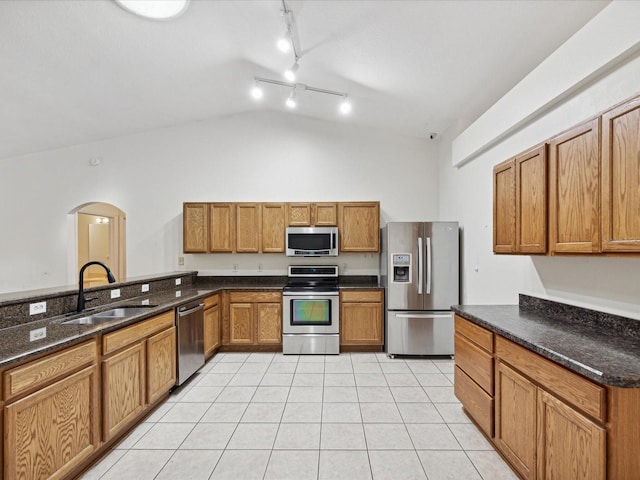 kitchen featuring sink, stainless steel appliances, vaulted ceiling, dark stone counters, and light tile patterned floors