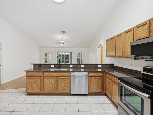 kitchen featuring kitchen peninsula, stainless steel appliances, sink, and dark stone counters