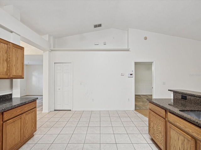 kitchen with vaulted ceiling, light tile patterned flooring, and dark stone counters