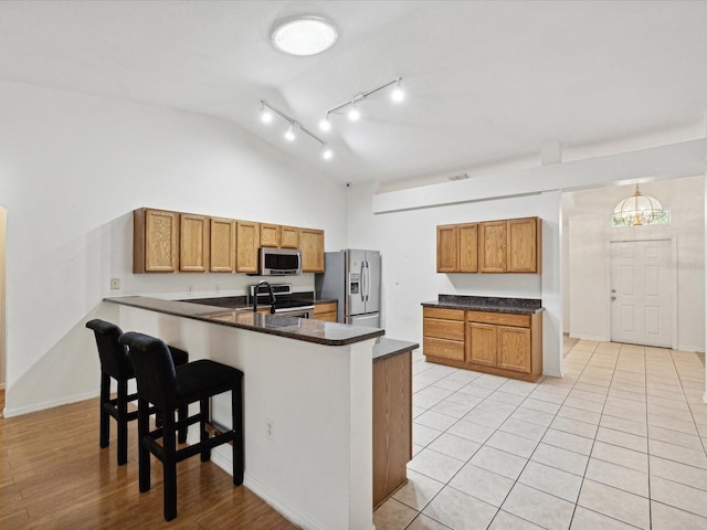 kitchen with appliances with stainless steel finishes, light wood-type flooring, kitchen peninsula, lofted ceiling, and a breakfast bar area