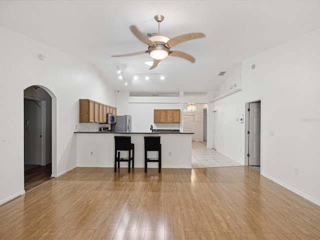 kitchen with appliances with stainless steel finishes, kitchen peninsula, light hardwood / wood-style floors, high vaulted ceiling, and a breakfast bar area