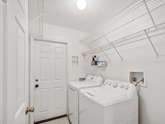 laundry room with a textured ceiling, washing machine and dryer, and light tile patterned floors