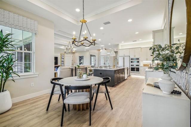 dining space with sink, a tray ceiling, ornamental molding, light hardwood / wood-style flooring, and a chandelier