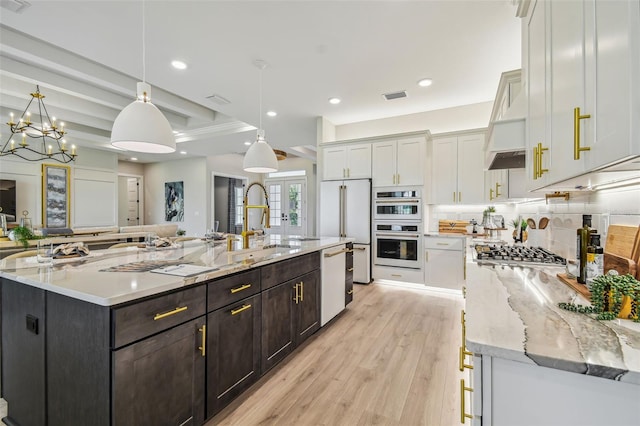 kitchen with a large island, light stone countertops, hanging light fixtures, and stainless steel appliances