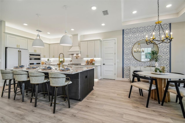 kitchen featuring custom range hood, stainless steel appliances, hanging light fixtures, and an island with sink