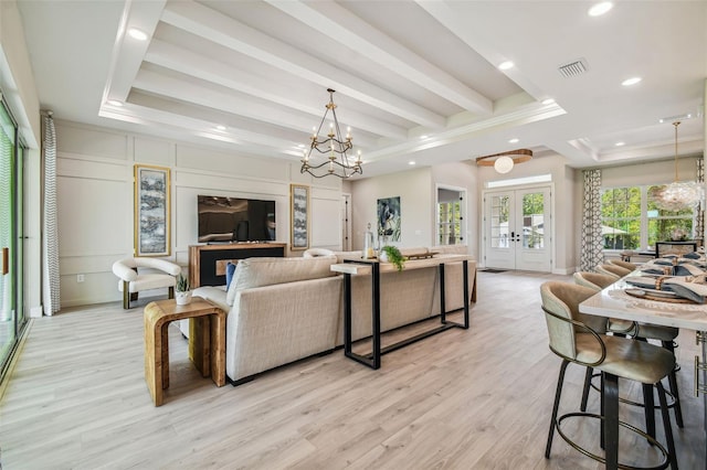 living room featuring french doors, a tray ceiling, beam ceiling, light hardwood / wood-style flooring, and an inviting chandelier