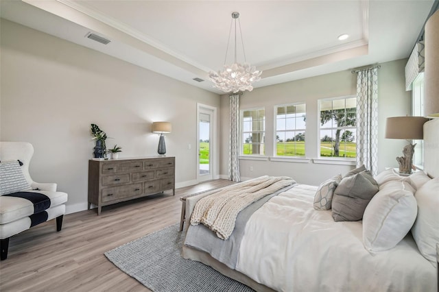 bedroom with ornamental molding, a chandelier, light wood-type flooring, and a raised ceiling