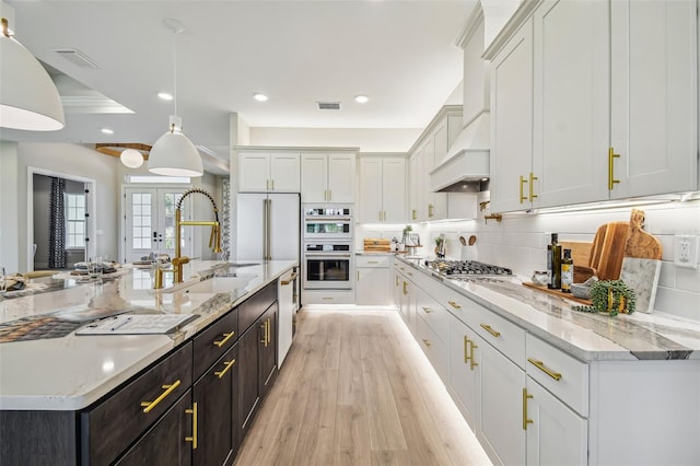 kitchen featuring premium range hood, white cabinets, decorative light fixtures, and light wood-type flooring