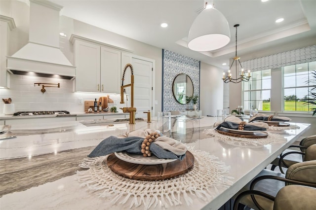 kitchen featuring a kitchen breakfast bar, light stone countertops, decorative light fixtures, stainless steel gas stovetop, and premium range hood