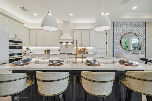 kitchen with custom exhaust hood, light stone countertops, and pendant lighting