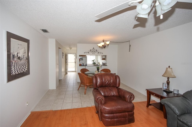 living room with a textured ceiling, light hardwood / wood-style flooring, and ceiling fan with notable chandelier