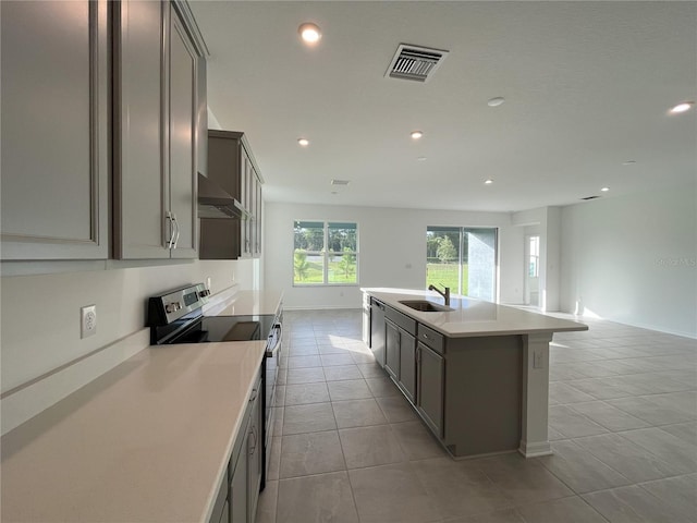 kitchen featuring wall chimney range hood, an island with sink, sink, light tile patterned floors, and appliances with stainless steel finishes