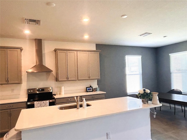 kitchen with dark tile patterned flooring, wall chimney exhaust hood, an island with sink, sink, and stainless steel electric range oven