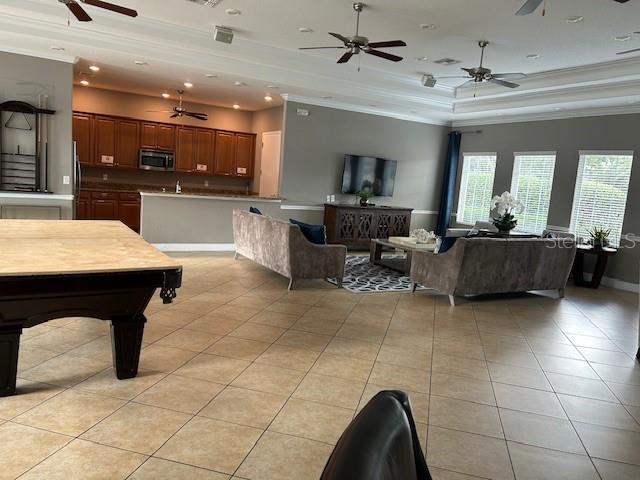 living room featuring crown molding, a raised ceiling, light tile patterned floors, and pool table