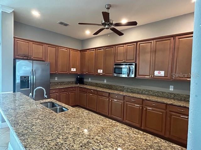 kitchen with light stone countertops, appliances with stainless steel finishes, sink, and ceiling fan