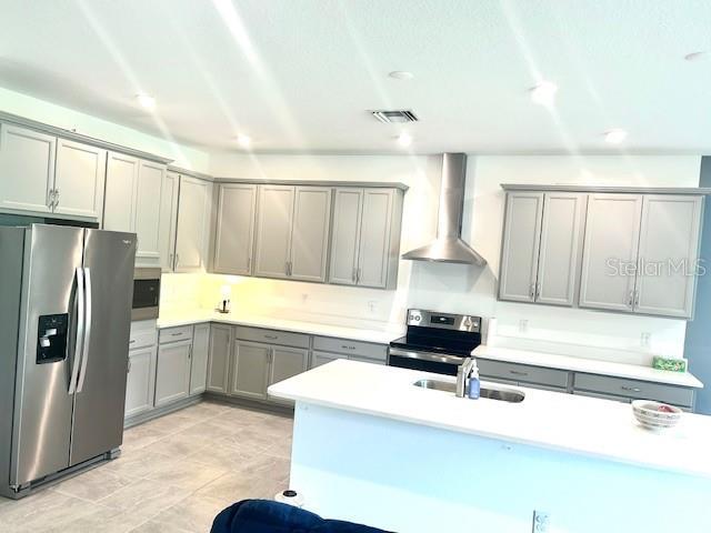 13447 Newport Shores Dr, Hudson, FL 34669 - kitchen with stainless steel appliances, wall chimney range hood, gray cabinets, light countertops, and recessed lighting