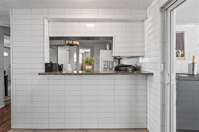 bar featuring dark stone counters, white fridge, wood-type flooring, and a textured ceiling